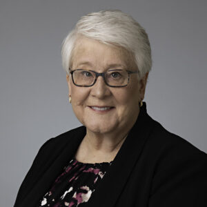 Portrait of Susan Coler, attorney, smiling at the camera while wearing a black suit and matching glasses.